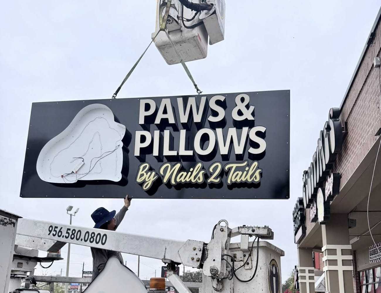 Paws & Pillows sign being installed on a storefront by workers using a lift.